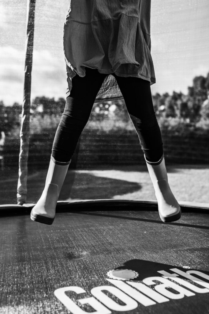 Girl jumping on trampoline in gumboots, cropping at the hips