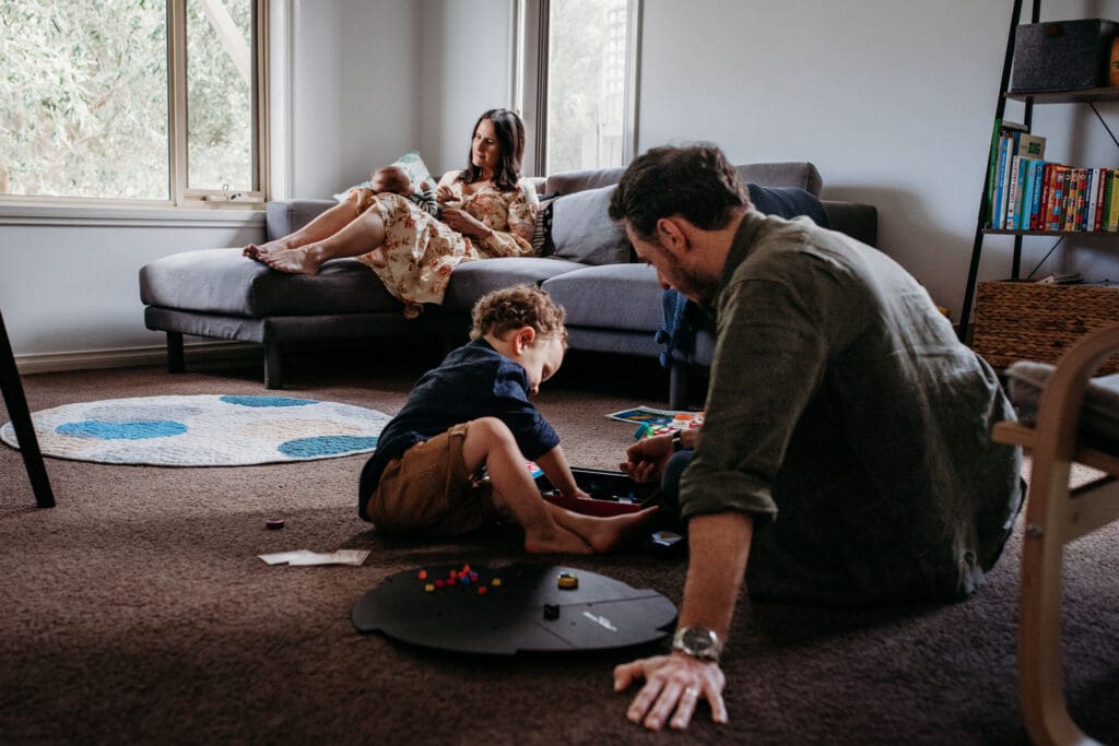 Mother playing with baby while dad and son play on the floor. 