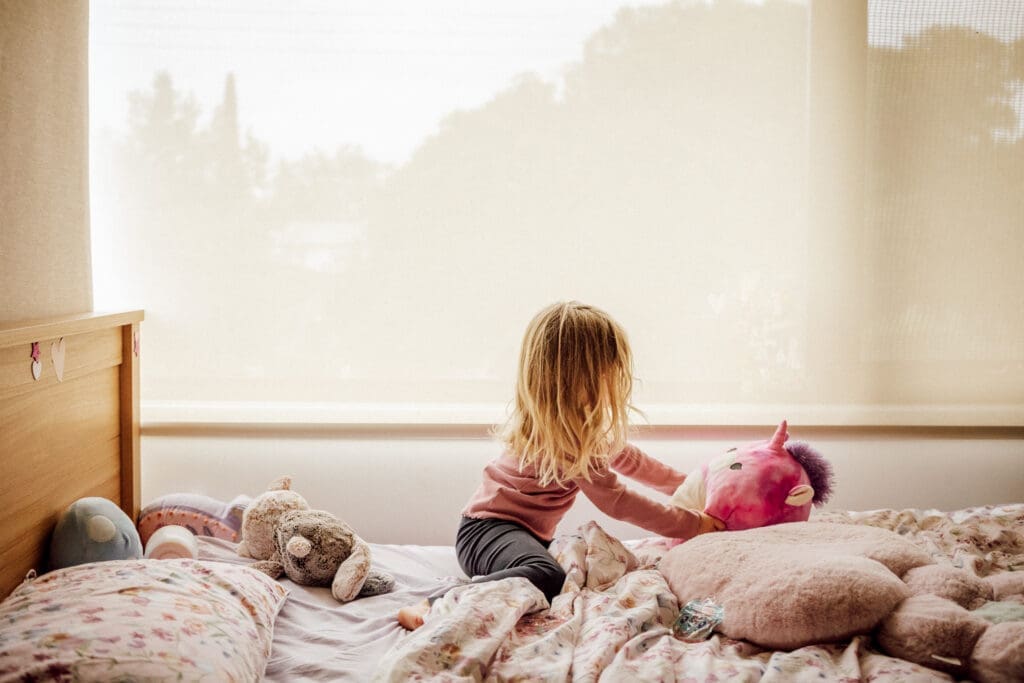 Young girl playing with toys, including a Squishmallow, on her bed. 