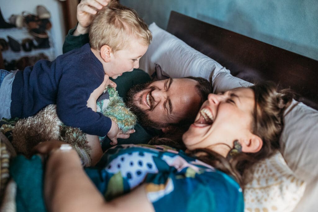 Little boy jumping on parents in their bed. 