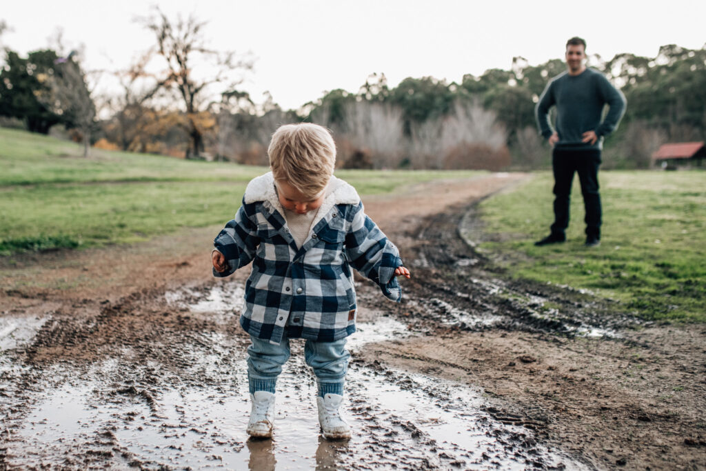 Parent wishing they dressed their child in gumboots as they wear their new white sneakers in a muddle puddle.